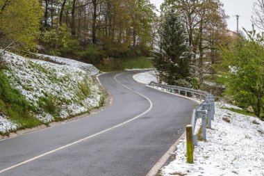 Karla kaplı bir ormanın içinden geçen asfalt bir yol.