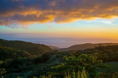 Monteverde, Kosta Rika 'da kırsal alanların ve dağların üzerinde altın gibi parlak bir günbatımı manzarası.