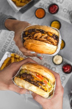 Lezzetli hamburgerleri soslu bir masanın üzerinde tutarken dikey bir fotoğraf.