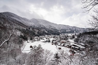 Dağlarla ve kışın karla kaplı ağaçlarla çevrili bir köyün manzarası.