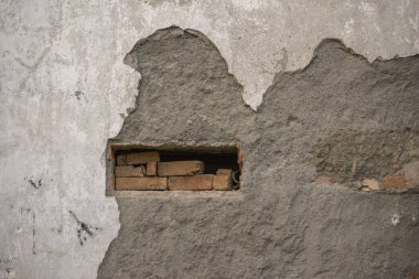 Deliğinde tuğlalar olan hasarlı bir beton duvar.