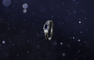 Soyut bir arkaplanda mavi taşlı bir yüzüğün yakın plan çekimi.