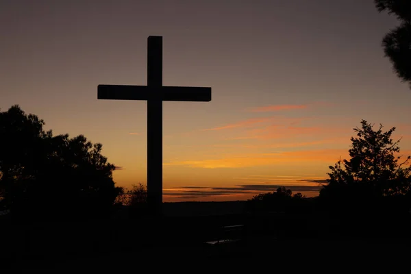 A beautiful shot of a backlit cross silhouette amongst trees with an orange sunset in the background
