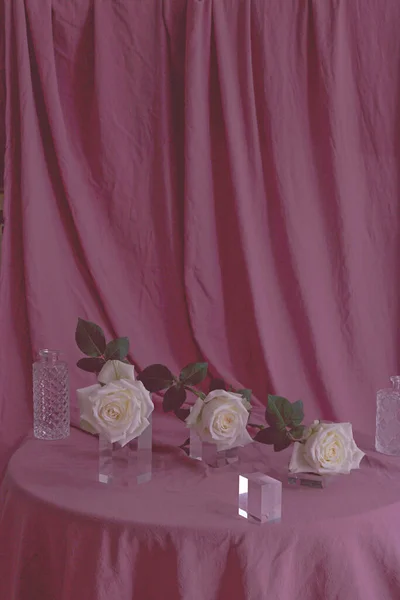 Вертикальный Снимок Белых Роз Красивыми Стеклянными Бутылками Розовой Поверхности Ткани — стоковое фото