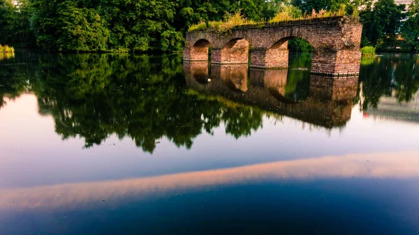穏やかな川に架かる古い壊れた橋で 水面には空と木々が反射しています — ストック写真