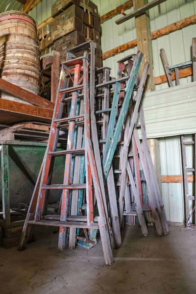 A vertical shot of old ladders leaning against a barn wall