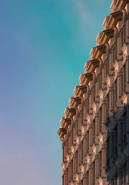 A vertical shot of a building facade in the background of the blue sky.