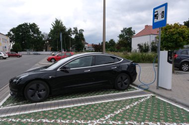 Bulutlu bir yaz gününde, siyah bir Tesla Model 3 çift motorlu AC şarj istasyonunun statik görüntüsü. Opole Voyvodalığı