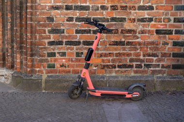 Tuğla duvarın yanına park edilmiş pembe bir scooter.