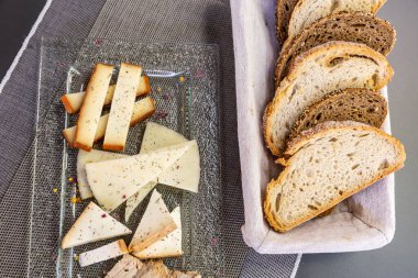 Farklı tipte peynirlerle dolu cam bir tabağın ve masanın üzerinde bir kase ekmeğin üst görüntüsü.