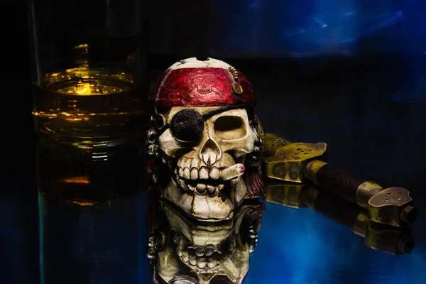 A closeup of a pirate skull with a sword and a whisky bottle on a blue reflective surface