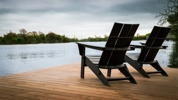 木々に囲まれた湖の岸にある2つの木製の椅子の風光明媚なショット — ストック写真