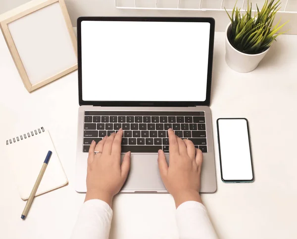 A top view of a person working on her laptop with a smartphone and a notepad on a desk