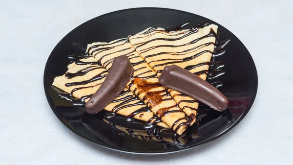 A closeup shot of crepes with chocolate syrup and candies on a black plate