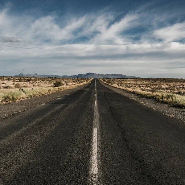 Kurak yolda asfalt yol mavi bulutlu bir arka plan üzerine iniyor.