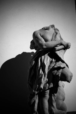 Duvarında gölgesi olan kafasız bir heykelin gri tonda dikey çekimi.