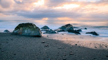 Gün batımında dalgalı denizin kayalık sahili.