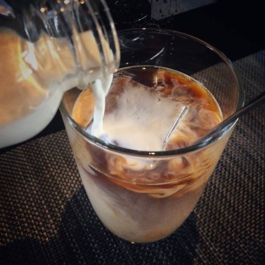 Taze süt eklerken bir bardak buzlu kahvenin yakın çekimi.