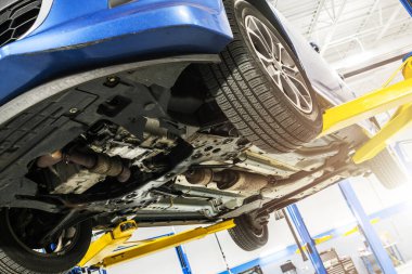 Otomotiv garajındaki asansörde bakım altında modern bir arabanın görüntüsü.