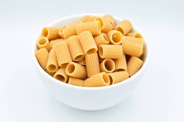 Beyaz arka planda beyaz bir kasede çiğ rigatoni makarnası.