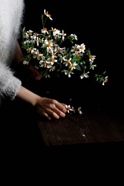 Koyu bir arka plana karşı tahta bir masada yatan çiçekleri toplayan bir kadının dikey yakın çekimi.