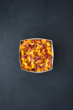 Gri bir yüzey üzerinde leziz peynirli pastırma konteynırının dikey üst görüntüsü.