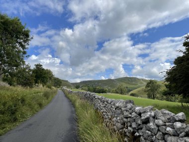 Yeşil tepeler ve bulutlu mavi gökyüzü olan taş bir duvar arasındaki güzel bir manzara.