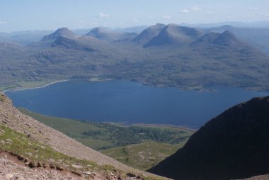 İskoçya 'da güneşli bir günde yeşil tepelerle çevrili sakin bir göl manzarası.