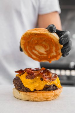 Eldivenli bir aşçının masada lezzetli bir burger hazırlarken dikey bir fotoğrafı.