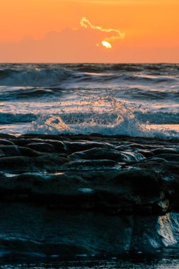 Gün batımında sahile vuran büyük dalgaların dikey görüntüsü.