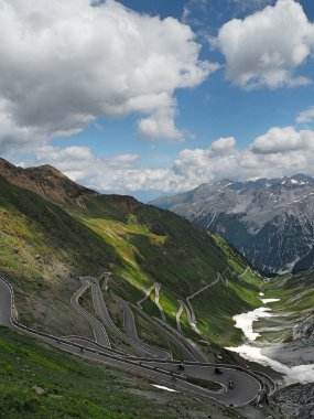 Güneşli bir günde mavi bulutlu bir gökyüzünün altında tepelerde ve dağlarda motosikletli bir yol.