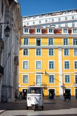 Küçük beyaz bir tuk-tuk şehir merkezinde büyük sarı binalar destekli, Lizbon Portekiz