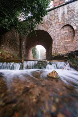 Kemerli bir taş köprünün altından akan nehrin dikey görüntüsü.