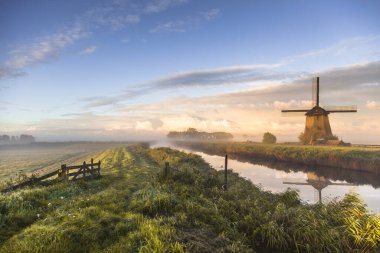 Bir yel değirmeni ve gün batımı gökyüzü bir nehirde yansıyor