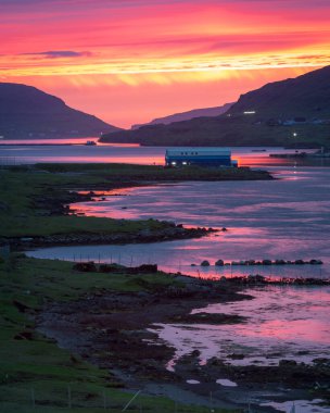 Sahile yakın bir su kütlesinin dikey görüntüsü. Arka planda çarpıcı renkli bir gökyüzü var.