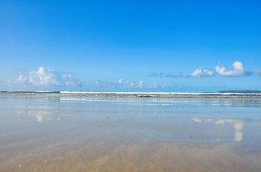 Denizin üzerindeki mavi gökyüzü yazın kumlu sahilde sakince süzülen dalgalarla.