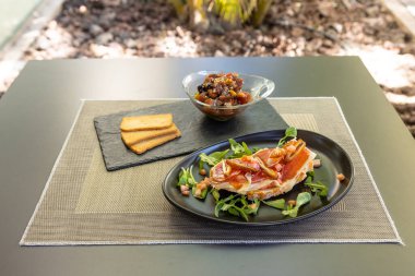 Siyah tabakta yeşil ve baharatlı bir et dilimi ve kasede lezzetli bir yemek.