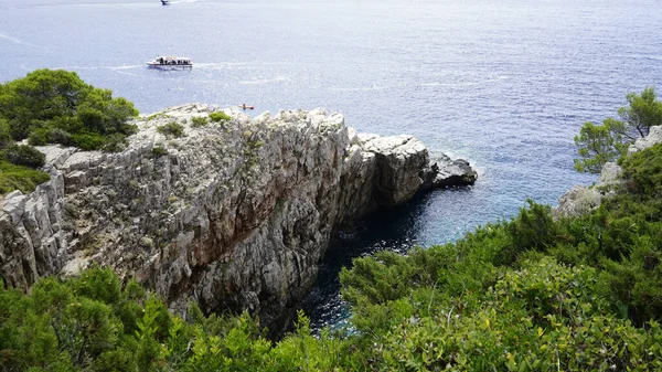 緑の木々に覆われた岩の崖に対して青い海を航海するボートの景色 — ストック写真