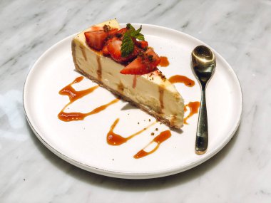 Beyaz tabakta çilekli bir dilim peynirli kekin yakın çekimi.