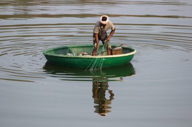 Suyun üzerinde yeşil bir teknede balık avlayan bir balıkçının yakın çekimi.