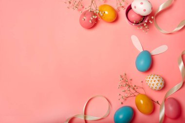 Renkli Paskalya yumurtalarının ve pembe arka plandaki dekorasyonların üst görüntüsü.