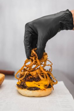 Eldivenli bir elin, ahşap bir masada lezzetli bir burger yaparken dikey çekimi.