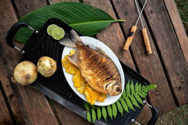 Piknik masasındaki siyah tahtada pişmiş balık ve kızarmış muz tabağının üst görüntüsü.