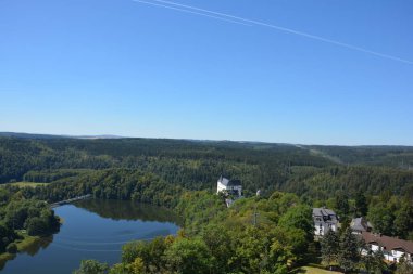 Yoğun bir ormanın, büyük bir havuzun ve birkaç evin manzaralı manzarası.