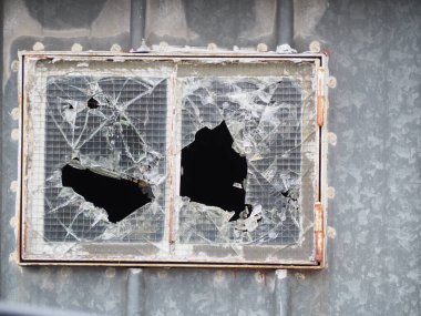 Güneşli bir günde, bir binanın ön cephesinin gri duvarında kırık bir cam pencerenin yakın plan çekimi.