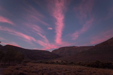 Güney Afrika 'da bir çayır ve dağların üzerinde büyüleyici bir günbatımı gökyüzü.