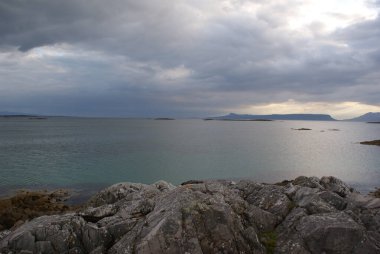 İskoçya 'da bulutlu bir gökyüzünün altında kayalık kıyı ve dağ manzarası