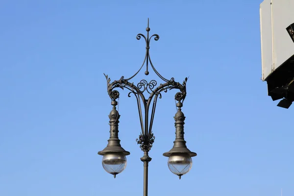 An antique-style black street lamp with the blue sky in the background