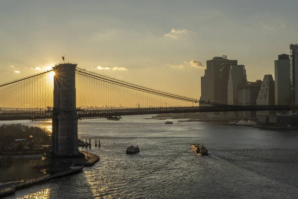 高層ビルや日当たりの良い空の背景に背の高いブルックリン橋の下の東の川 — ストック写真