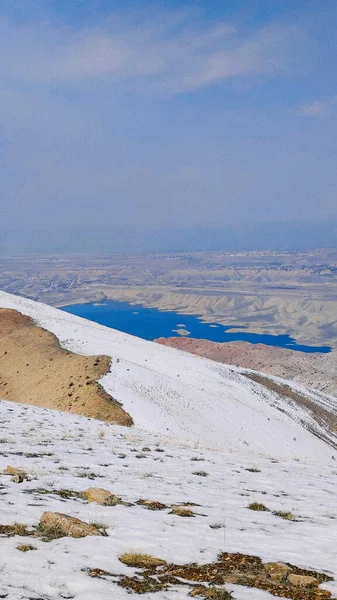 雪の丘の垂直ショットと明るい青空の下で小さな湖 — ストック写真